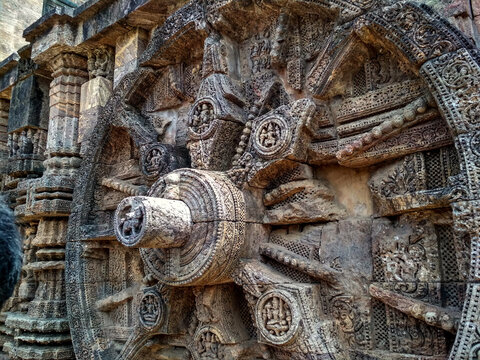 An ancient stone carving of a wheel in Konark Sun temple. The wheel is intricately designed with spokes and detailed patterns.