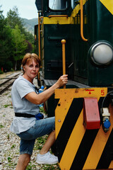 Female visitor on the steps of a green diesel locomotive at the Sargan Eight heritage railway. Woman travels in Mokra Gora, Serbia.