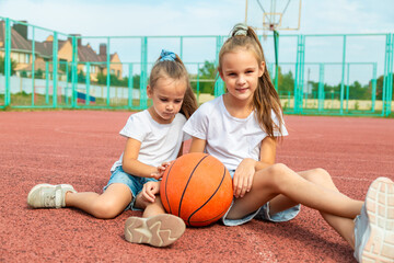 Children are sitting under a basketball basket on the playground with a basketball. Hobbies and active sports games