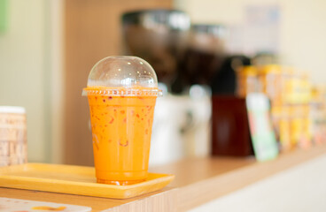 Iced Thai milk tea in a plastic cup on a wooden tray, placed on a cafe counter. A popular and...