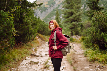 Female hiker with a backpack stands on mountain hiking trail and enjoys the mountain scenery on a...