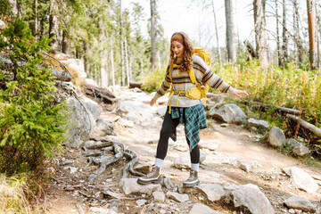 Female hiker with a colorful hiking backpack on a walking rocky trail in the mountains. Cute woman...