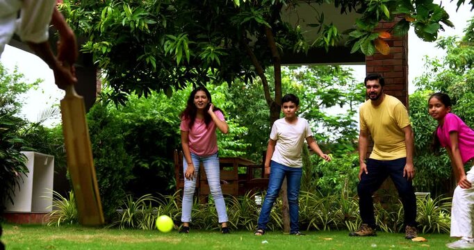 Indian family playing cricket bowling in home garden, spending quality fun time together with kids parents enjoying outdoor activity, cheerful Asian siblings and adults bonding during backyard match