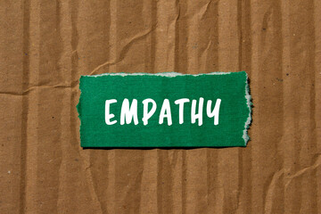 Empathy message written on ripped torn green paper piece on cardboard paper background. Conceptual...