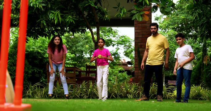 Indian family playing cricket bowling in home garden, spending quality fun time together with kids parents enjoying outdoor activity, cheerful Asian siblings and adults bonding during backyard match
