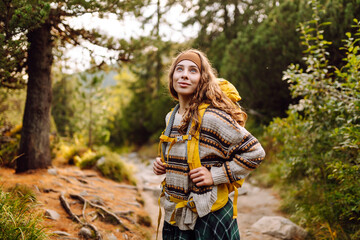 Female hiker with a colorful hiking backpack on a walking rocky trail in the mountains. Cute woman enjoying mountain scenery in a dense forest. Adventure, hiking and nature concept.