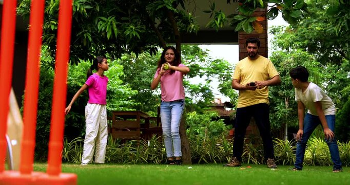 Indian family playing cricket bowling in home garden, spending quality fun time together with kids parents enjoying outdoor activity, cheerful Asian siblings and adults bonding during backyard match
