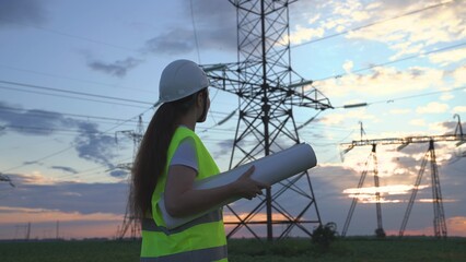 An electrician on the background of high towers of power plants looks at the project for the development of an electrical structure, the expansion of the electrical voltage of volts in the wires.