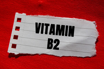 Vitamin B2 message written on ripped torn lined paper piece on red background. Conceptual Vitamin...