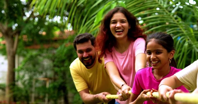 Indian family playing tug of war rassi khech in home garden, spending quality fun time together enjoying outdoor sports, cheerful Asian parents children bonding through traditional backyard activity