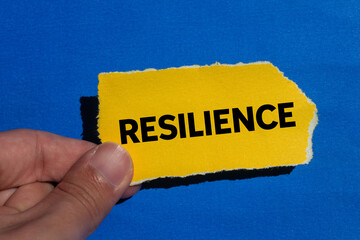 Resilience message written on ripped torn yellow paper piece on blue background. Conceptual...