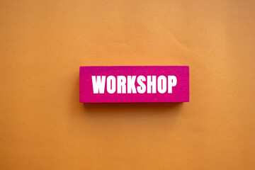 Workshop message written on pink wooden block on orange background. Conceptual Workshop symbol. Copy space.