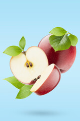 Bright red apples, green leaves closeup levitation as swirl on pastel blue background as art composition, whole, half, quarter fruit, shadow. Summer fruits for advertising, design, label product.