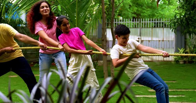 Indian family playing tug of war rassi khech in home garden, spending quality fun time together enjoying outdoor sports, cheerful Asian parents children bonding through traditional backyard activity