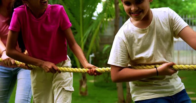 Indian family playing tug of war rassi khech in home garden, spending quality fun time together enjoying outdoor sports, cheerful Asian parents children bonding through traditional backyard activity