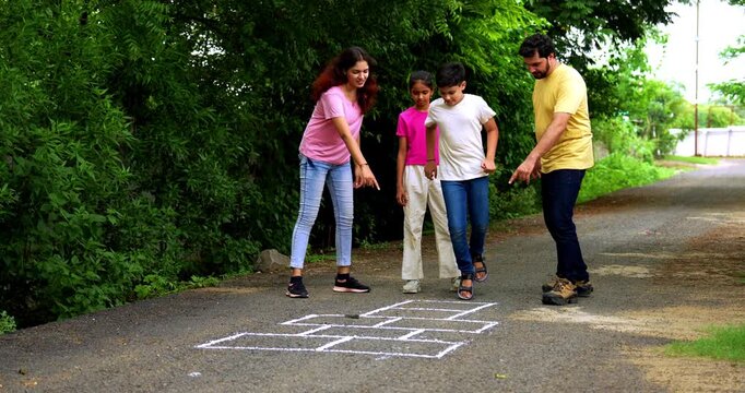 Indian family playing Tikkar Billa, a traditional hopscotch game in home garden, spending quality fun time together with children hopping on squares and enjoying nostalgic outdoor sports activity