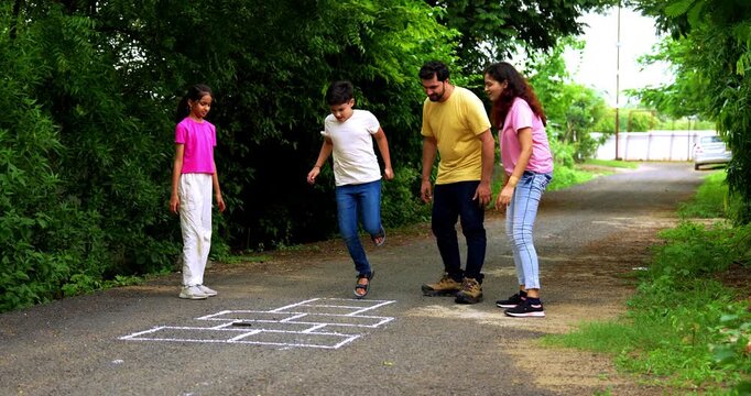 Indian family playing Tikkar Billa, a traditional hopscotch game in home garden, spending quality fun time together with children hopping on squares and enjoying nostalgic outdoor sports activity