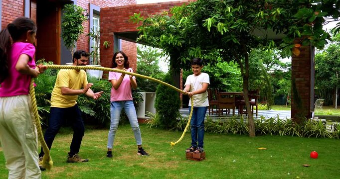 Indian kids playing tug of war or rassi khech in home garden while parents cheer them, spending quality fun time together enjoying traditional outdoor sports bonding during weekend family activity