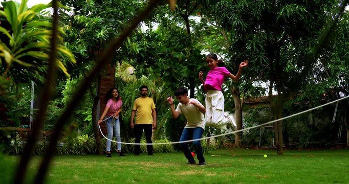 Indian family playing jumping rope in home garden, spending quality fun time together enjoying outdoor sports, cheerful Asian parents children bonding through traditional fitness activity in backyard