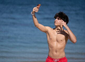 Portrait of confident young man taking a selfie with smartphone while enjoying a sunny day at the beach