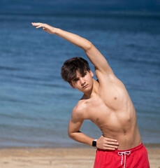 Portrait of young fitness man stretches his body on a sunny beach, enjoying the fresh air