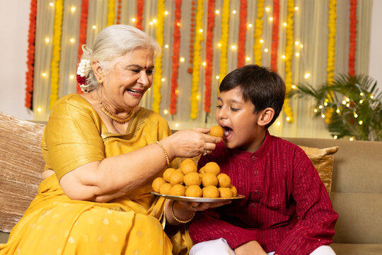 Indian grand mo Eating Diwali Laddu or laddoo Together Indoors the occasion of Decorated Home with Lights During Diwali festival