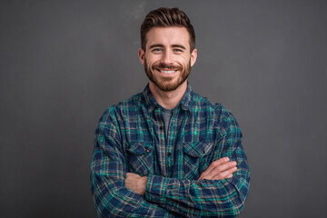 Smiling Young Man in Blue and Green Plaid Shirt with Arms Crossed on Gray Background

