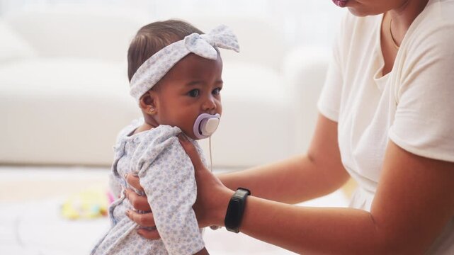 Mother holds baby girl with a pacifier, providing comfort and security during family bonding, making family bonding a loving and reassuring daily moment in a warm home setting.