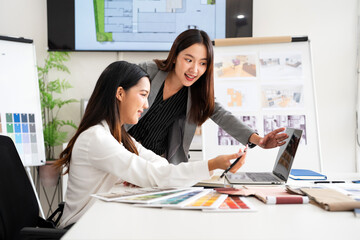 Professional young interior designers and architects working together in the office, they are using a laptop and considering material samples.
