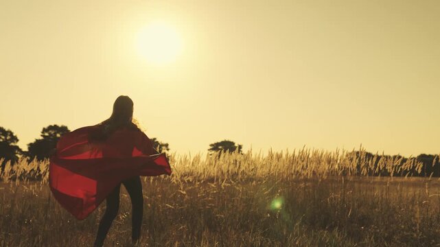 happy teenage girl in developing red cloak in wind at sunset in the sky, dreaming of becoming superhero protecting weak and not wine people, defeating evil, good person who does good loves to help.