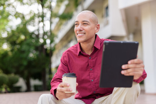 Bald man using digital tablet while sitting outdoors with coffee on stairs