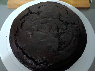 Whole homemade chocolate cake with a smooth top and dense texture, perfect for decorating or serving plain. Dark and rich, freshly baked.