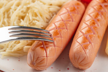 Close-up of grilled sausages with crosshatch cuts served alongside pasta and touched by a fork