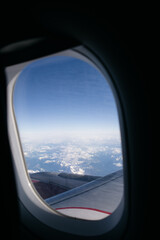 Fototapeta premium Airplane wing flying over snowy mountain tops seen through window