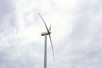 Wind turbine turn by cloudy sky close up, side view