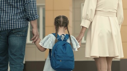 little girl goes hand in hand with parents to school, kid with a backpack on his back, teaching in elementary school, teaching knowledge of the school educational program, happy family.
