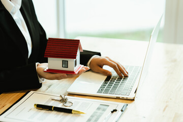 A real estate agent holds a house model and signs documents, symbolizing property sale, home...