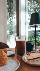 A Fruit juice glass, a mug of coffee, a Brazilian coxinha snack on a plate, and a slice of cake with chocolate sauce on a café table 