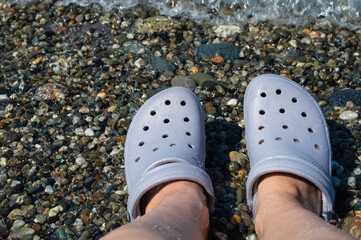 women's feet in clogs on the beach by the sea