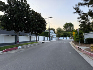 residential street in the city at sunset (trees, sidewalk, lawn, houses, walls, fence, utility pole with telephone wires, street signs) - Encino, Los Angeles, California, USA