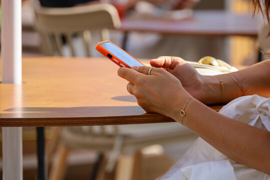 Smartphone in female hand on a street. Woman using mobile phone sitting at the cafe table in summer city