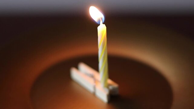 Una toma de cerca de una vela blanca con amarillo de cumplea&ntilde;os  con llama colocada en un gancho de madera en un fondo oscuro  