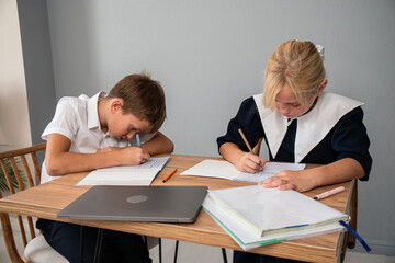 Children School Homework Studying - Two children are sitting at a table and writing in their notebooks. A laptop is on the table, suggesting they may be doing homework.