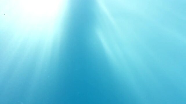 Underwater view of sun rays shinning through the surface of the water with twinkling bubbles. Abstract water background. Light rays shinning through blue water