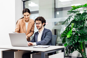 A business man and woman discuss ideas and learn new strategies in a modern office with a laptop....