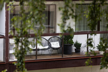 Cozy glazed balcony in Tallinn with modern black chairs, soft cushions, potted plants, and a transparent umbrella. Perfect outdoor relaxation space, ideal for urban lifestyle and home design themes.