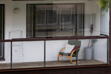 Minimalist glazed balcony in Tallinn with wooden chair, cozy cushions, and simple home details....