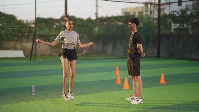 Indian young adult gen z woman lady jump on skip rope work out for weight lose. fit man gym trainer male guy coach watch sports female girl do daily health care learn good habit game garden place area