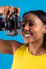 Young photographer using vintage camera smiling on blue background