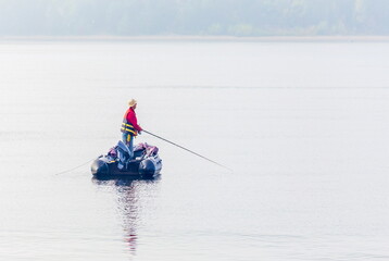 men Fisherman catches fish standing on an inflatable boat in the Volga River against the backdrop of the Zhiguli Mountains on a warm summer day